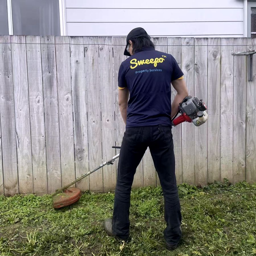 Sweepo team member line-trimming along a fence